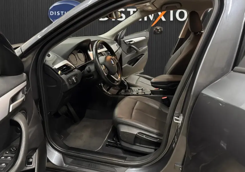 Vue intérieure côté conducteur d’un BMW X2 gris minéral métallique de 2019 avec sièges cuir noir et tableau de bord moderne.