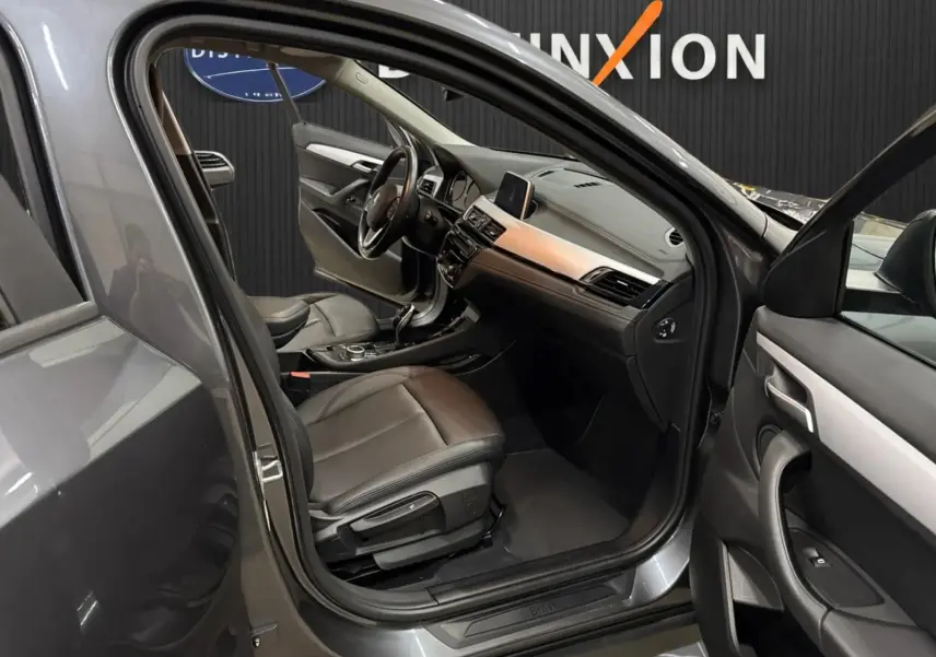 Vue intérieure côté conducteur d'une BMW X2 16dA Lounge Plus gris minéral métallique avec sièges cuir noir et tableau de bord moderne.