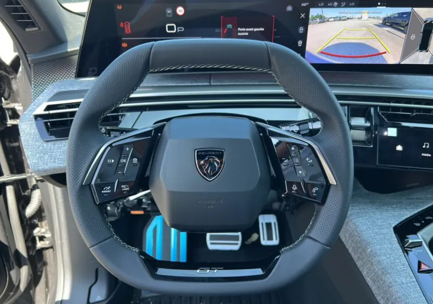 Vue rapprochée du volant cuir multifonctions GT de la Peugeot 3008 Hybrid 145, avec tableau de bord digital et caméra 360° affichée.