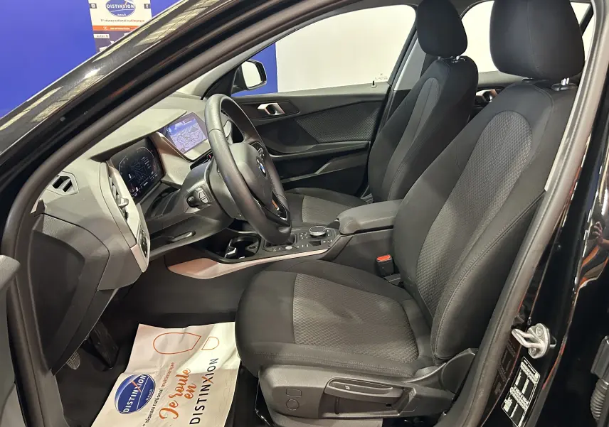 Vue intérieure côté conducteur de la BMW Série 1 noire 2023 avec sièges tissu et tableau de bord digital.