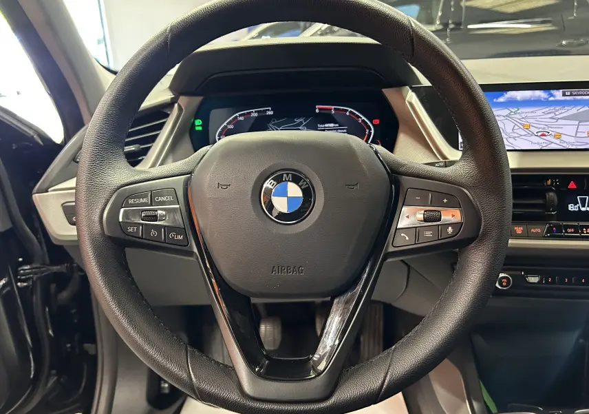 Vue rapprochée du volant noir de la BMW Série 1 16d 2023 avec tableau de bord numérique et écran GPS intégré.