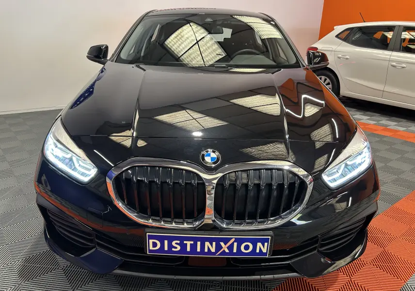 Vue de face d'une BMW Série 1 noire 16d 116ch avec phares LED allumés et calandre double haricot chromée.