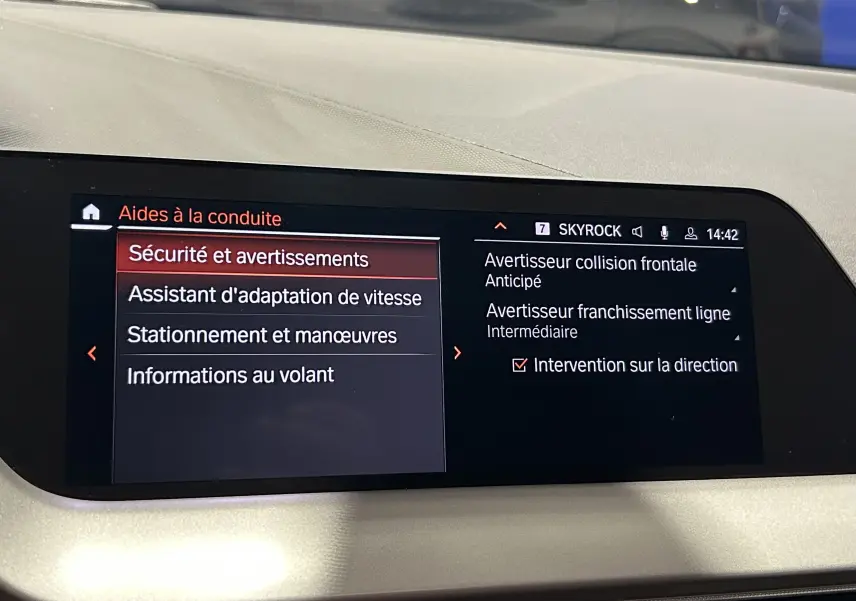 Écran central de la BMW Série 1 16d 2023 affichant les aides à la conduite et alertes de sécurité en intérieur noir.