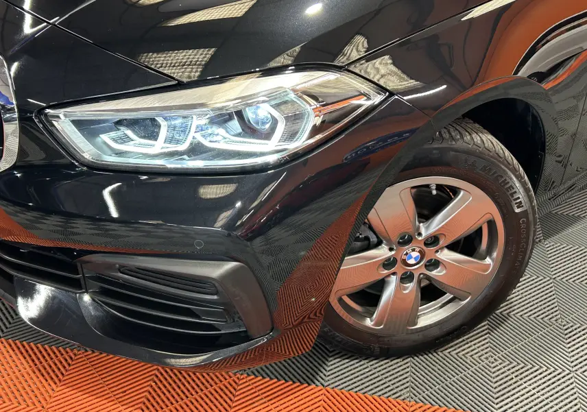 Gros plan sur l'avant droit noir d'une BMW Série 1 16d 2023, mettant en valeur le phare LED et la jante alliage.
