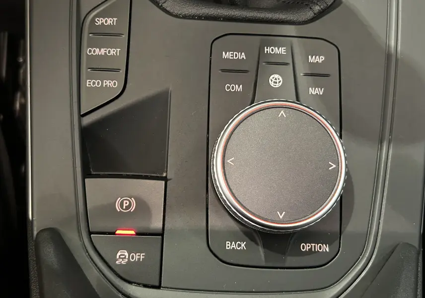 Gros plan sur la molette de commande centrale et les boutons de modes de conduite dans l'habitacle noir d'une BMW Série 1 16d 2023.