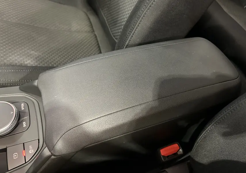 Accoudoir central en cuir noir avec commandes de la console sur BMW Série 1 16d 2023, vue rapprochée intérieure.