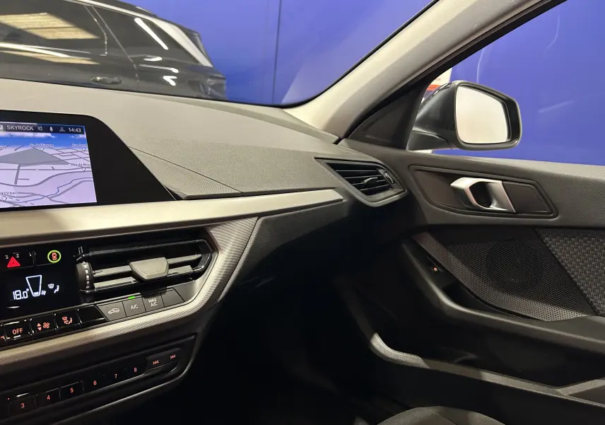 Vue intérieure côté passager de la BMW Série 1 noire 2023, mettant en valeur le tableau de bord avec GPS et les finitions modernes.