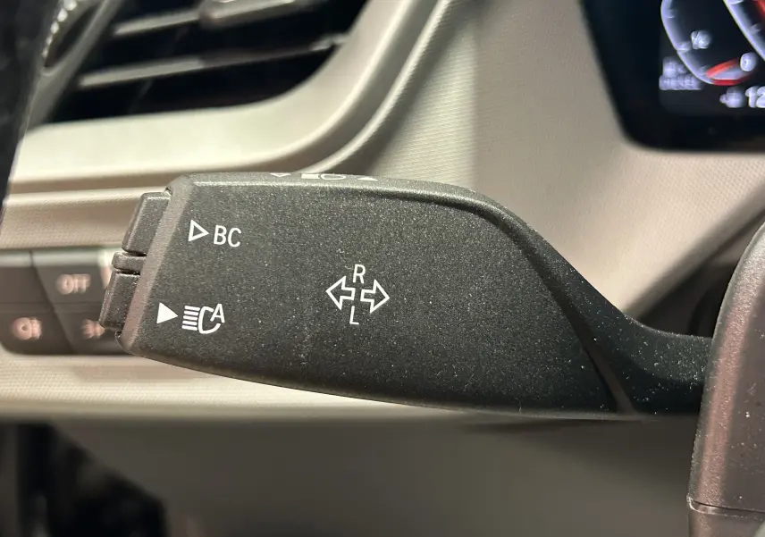 Le levier de clignotant noir de la BMW Série 1 16d 2023, avec commandes BC et feux automatiques visibles en gros plan.