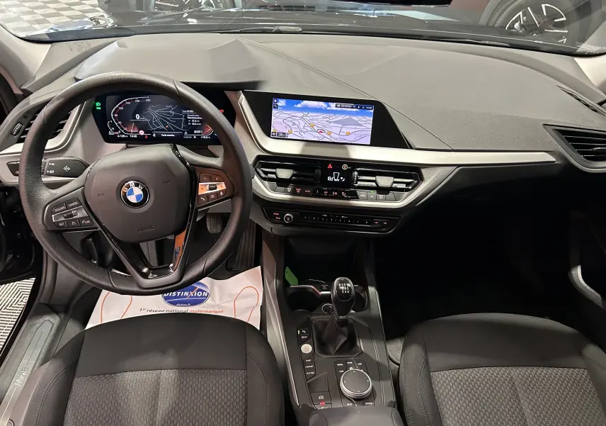 Intérieur BMW Série 1 16d 2023 en vue frontale, tableau de bord noir avec écran GPS et boîte manuelle visible.