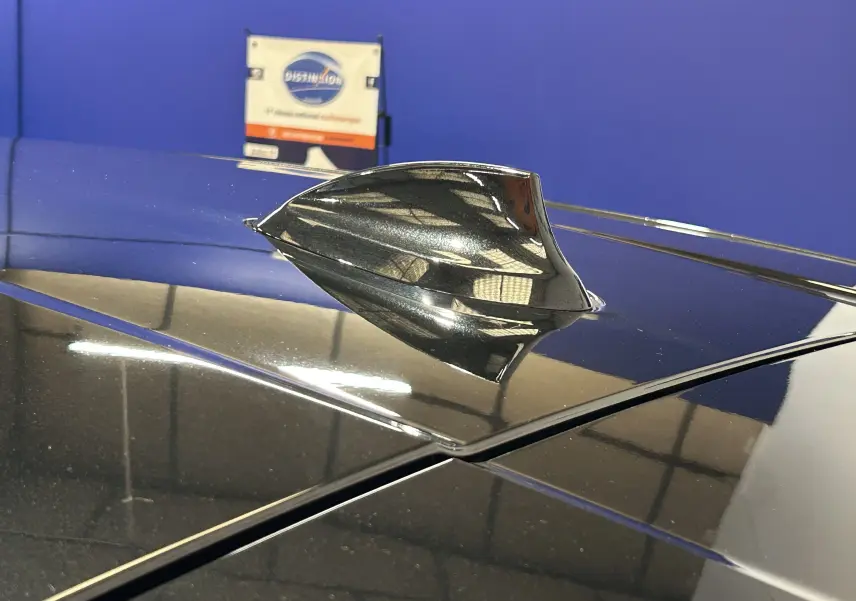 Gros plan sur l'antenne requin noire sur le toit d'une BMW Série 1 16d 2023, reflet d'atelier visible.