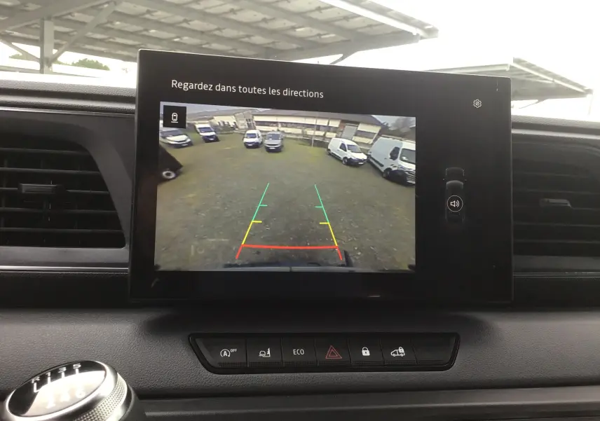 Vue intérieure du tableau de bord du Renault Master 2025, écran de caméra de recul affichant un parking avec plusieurs véhicules blancs.