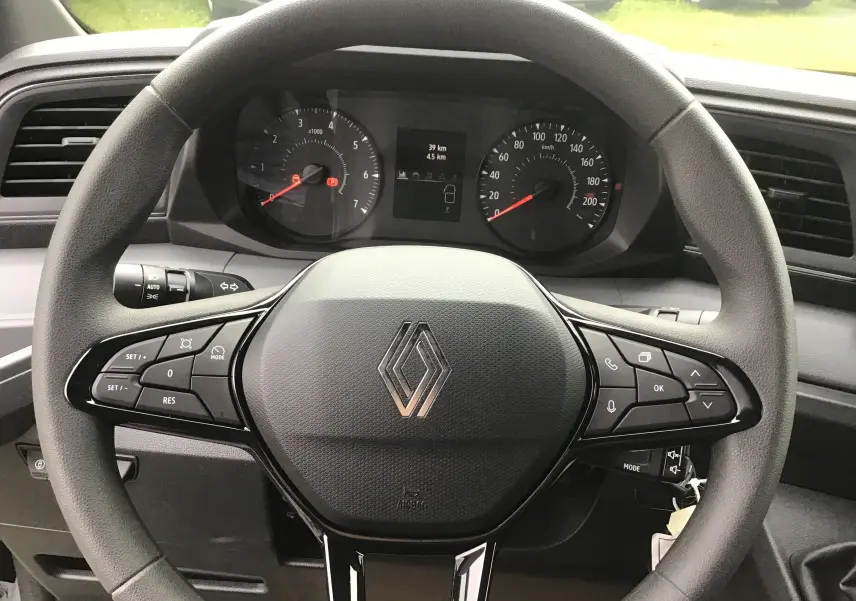 Vue rapprochée du volant noir du Renault Master 2025 avec commandes intégrées et tableau de bord digital en arrière-plan.