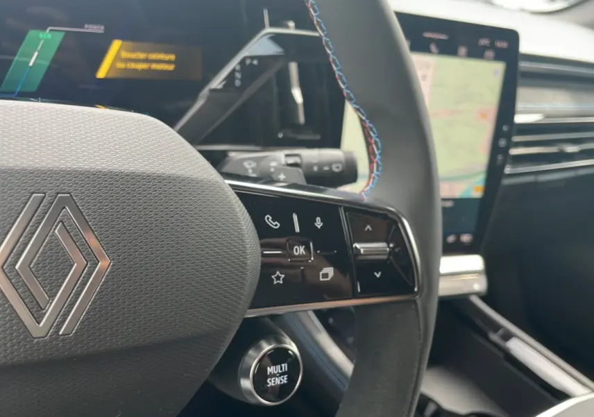 Gros plan sur le volant cuir multifonctions du Renault Austral gris schiste, avec commandes et écran tactile en arrière-plan.