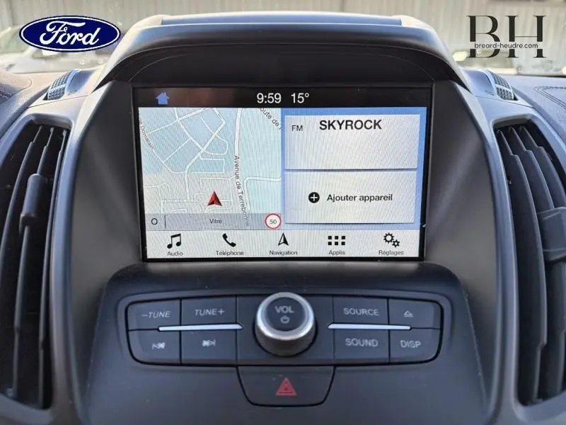 Vue rapprochée de l’écran tactile central du Ford Kuga blanc, affichant la navigation et la radio Skyrock.