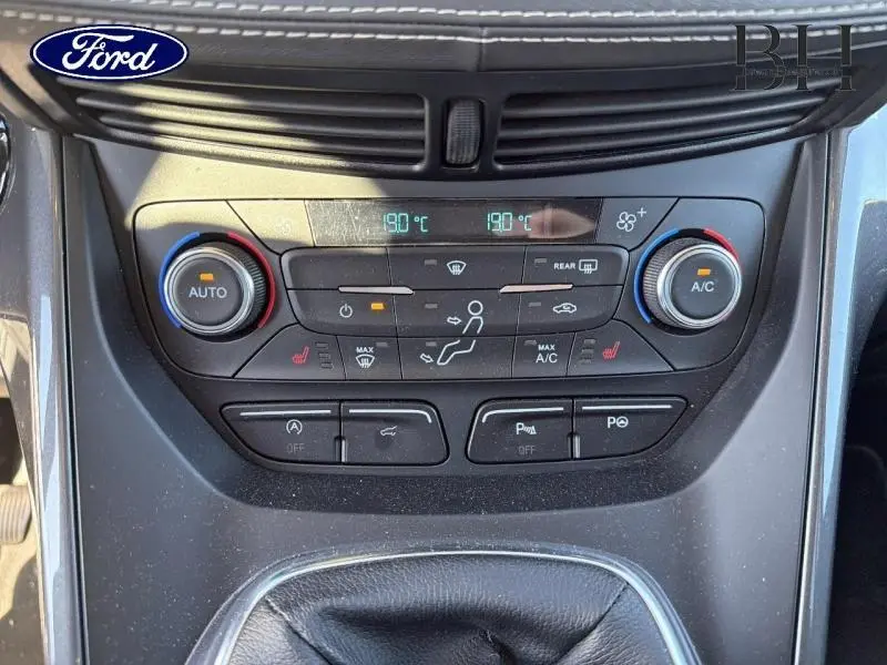 Vue rapprochée du tableau de bord central du Ford Kuga blanc, montrant les commandes de climatisation bi-zone et les boutons multifonctions.