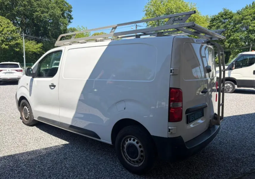 Vue 3/4 arrière gauche du fourgon blanc Peugeot Expert L1H1 Confort avec galerie de toit et porte-échelle arrière.