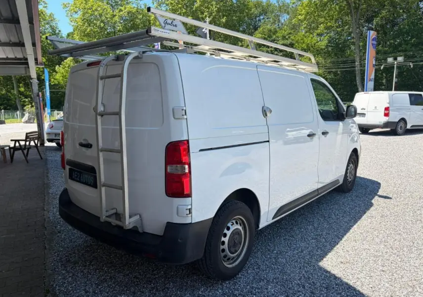 Vue 3/4 arrière droite du Peugeot Expert Fourgon blanc avec galerie et échelle sur le toit, stationné sur gravier.