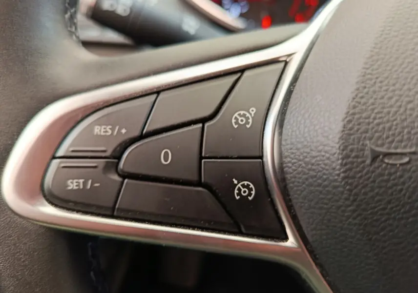 Gros plan sur les commandes du régulateur de vitesse au volant cuir synthétique d’une Renault Clio Business gris clair.