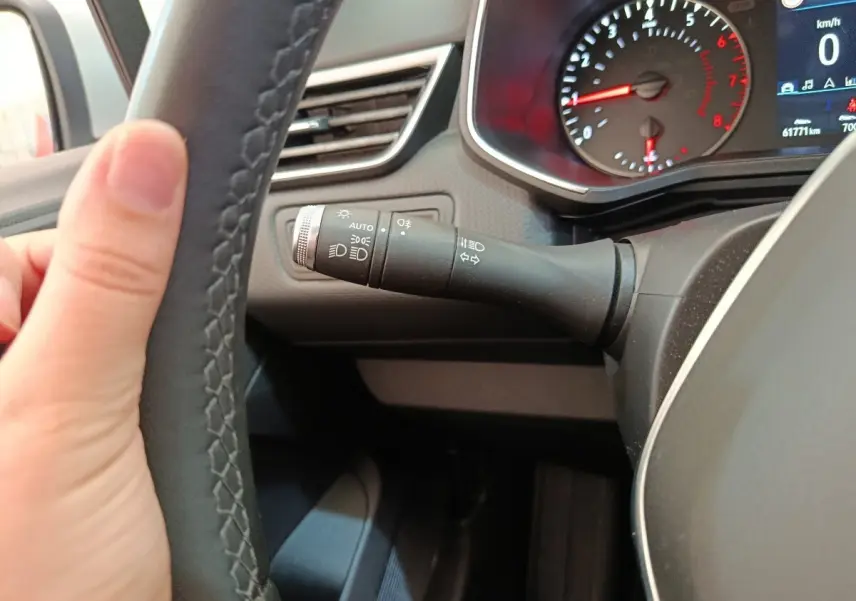 Gros plan sur le volant cuir synthétique et la manette des phares dans le tableau de bord de la Renault Clio Business gris clair.