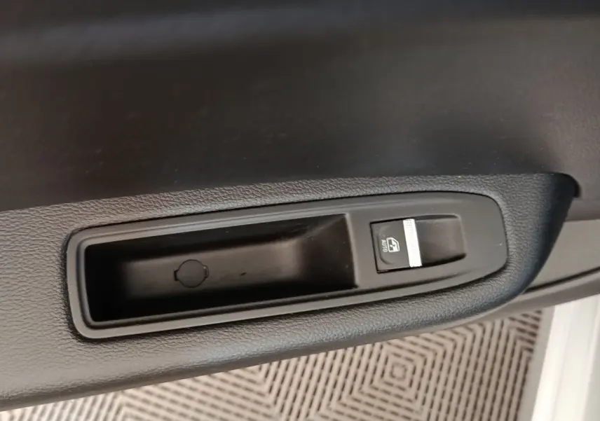 Gros plan sur le bouton de verrouillage centralisé noir dans l'accoudoir intérieur d'une Renault Clio gris clair.