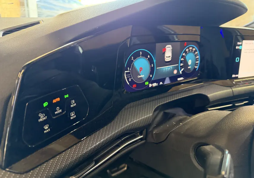 Vue rapprochée du tableau de bord numérique et des commandes d’éclairage sur la gauche dans une Volkswagen Golf blanche 2023.