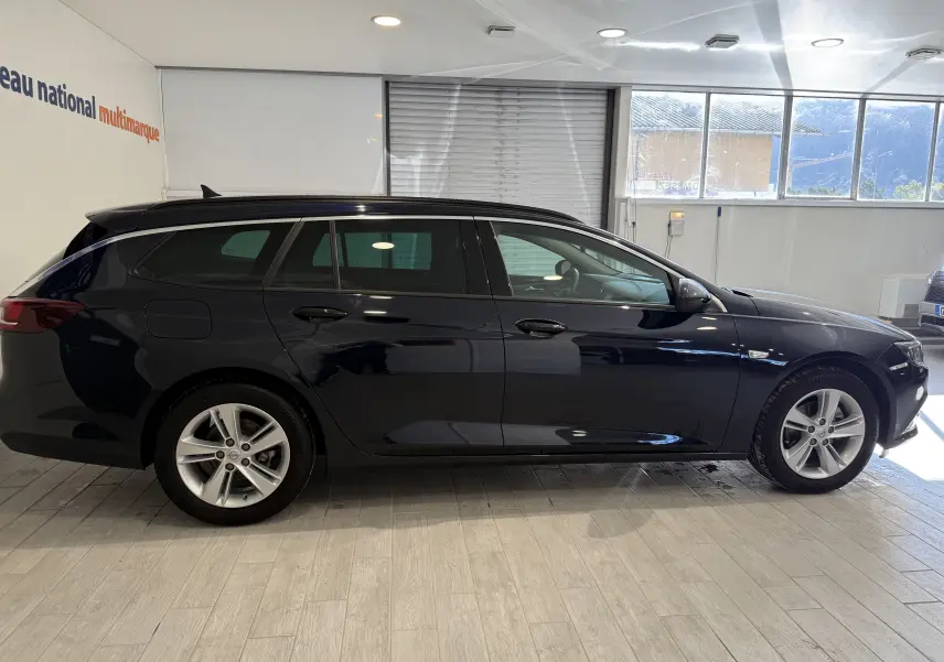 Profil latéral droit d'une Opel Insignia Sports Tourer bleu lune marine métal, break élégant en intérieur showroom.