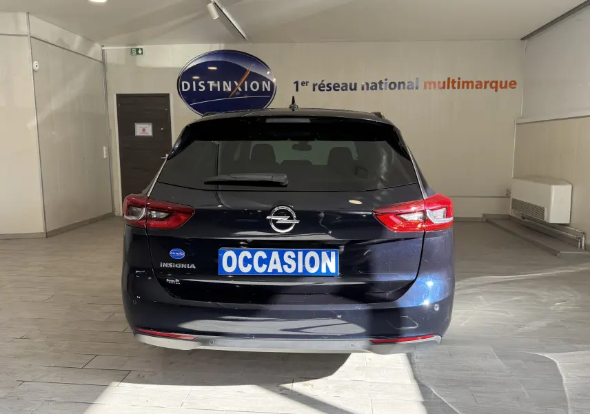 Vue arrière d'une Opel Insignia Sports Tourer bleu lune marine métal, avec feux arrière allumés en intérieur showroom.