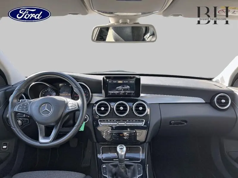 Vue intérieure avant de la Mercedes Classe C 200 d Business 2016 avec tableau de bord noir et volant multifonction cuir.