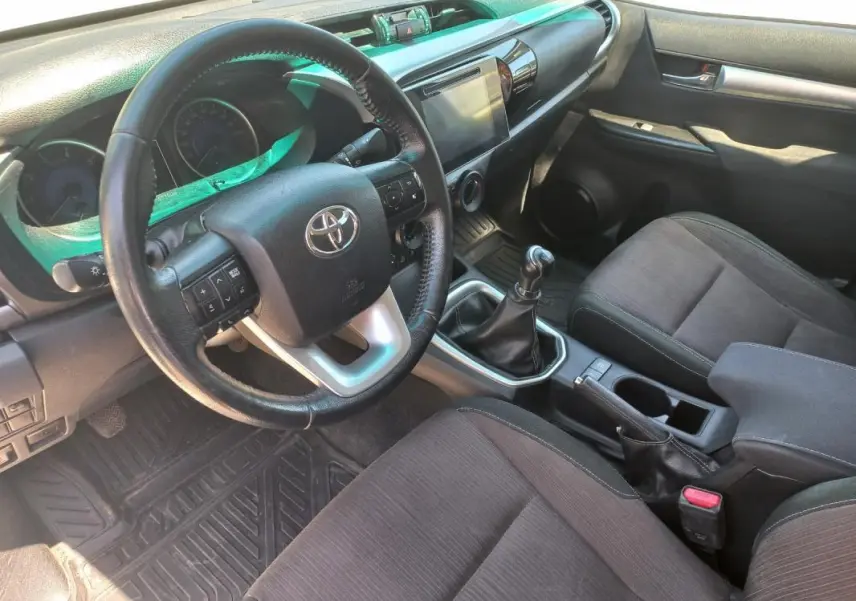 Vue intérieure côté conducteur du Toyota Hilux 2018, montrant le volant, la boîte manuelle et les sièges noirs.