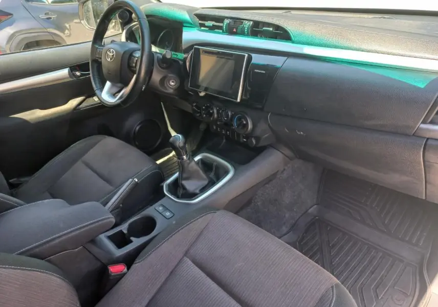 Vue intérieure côté conducteur du Toyota Hilux 2018, montrant le volant, la console centrale avec boîte manuelle et écran tactile.