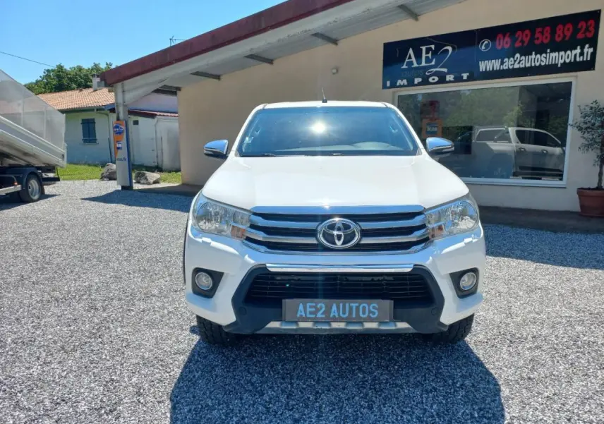 Vue de face du Toyota Hilux blanc 2018, double cabine, avec calandre chromée et plaque AE2 AUTOS.