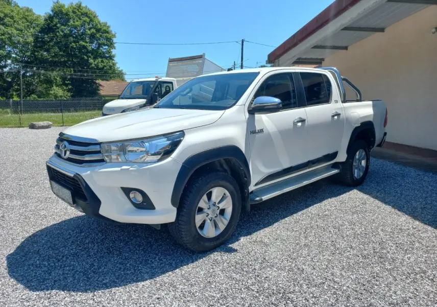 Toyota Hilux 4x4 blanc en 3/4 avant droit, double cabine avec barres de protection et jantes alliage.
