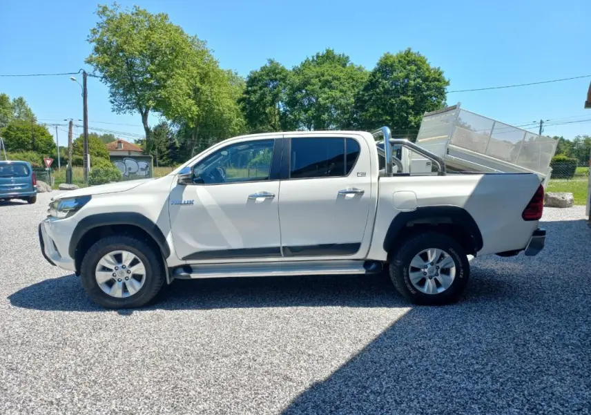 Profil droit du Toyota Hilux 4x4 blanc double cabine 2018 avec barres de protection et benne arrière relevée.