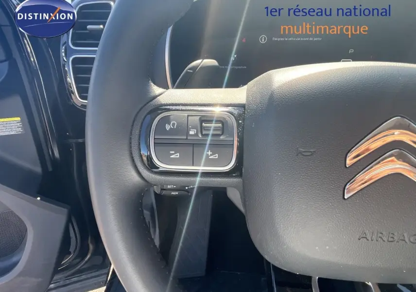 Gros plan sur le volant cuir noir du Citroën C5 Aircross 2025, avec commandes intégrées et logo chromé visible.