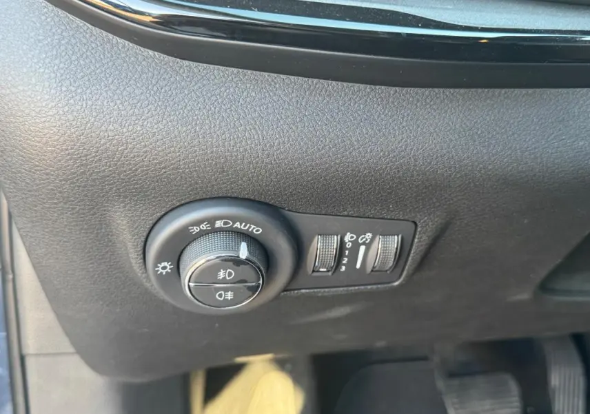 Gros plan sur le tableau de bord noir du Jeep Compass 2025, montrant les commandes d’éclairage et réglages des phares.