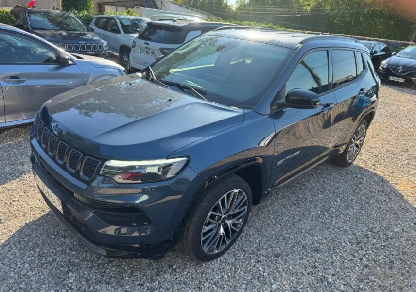 Vue 3/4 avant droite d'un Jeep Compass bleu 2025 avec jantes alliage 19 pouces et barres de toit visibles.