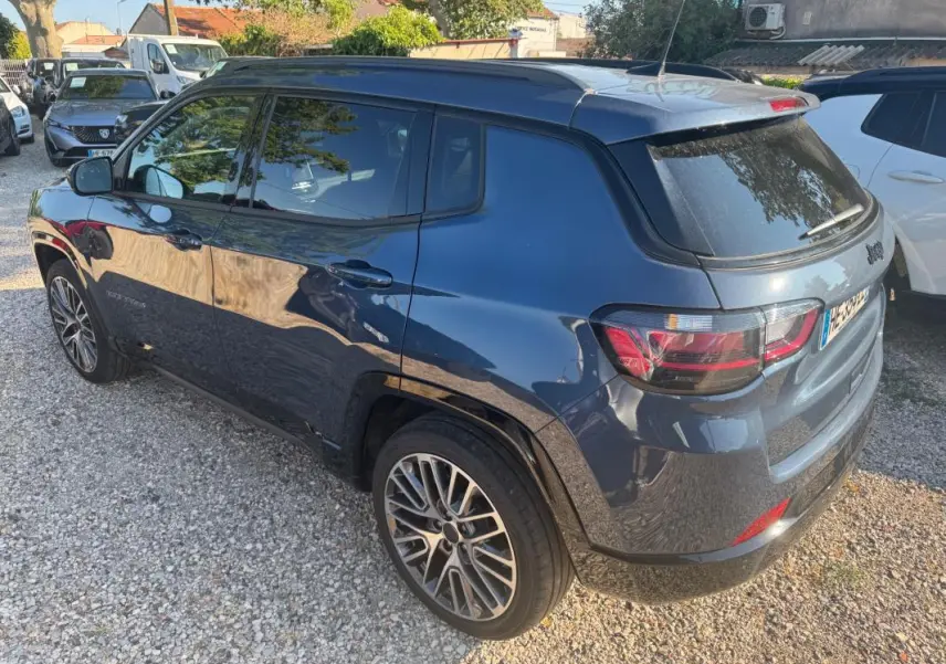 Vue 3/4 arrière droite d'un Jeep Compass bleu 2025 avec jantes alliage 19 pouces et barres de toit visibles.