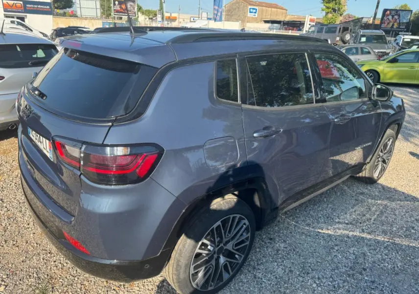Vue 3/4 arrière droite d’un Jeep Compass bleu 2025 avec jantes alliage 19 pouces et barres de toit visibles.