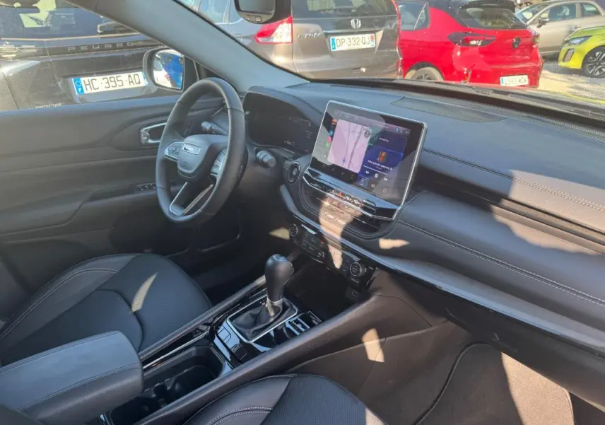 Intérieur avant droit du Jeep Compass bleu 2025, avec écran tactile, volant multifonction et accoudoir central.