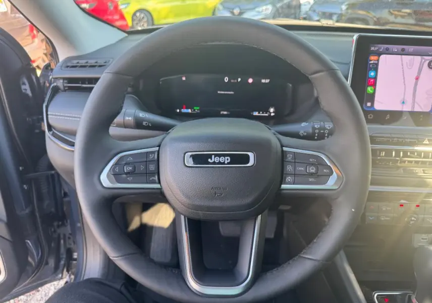 Vue centrée du volant noir du Jeep Compass 2025 bleu, avec tableau de bord numérique et écran tactile visible à droite.