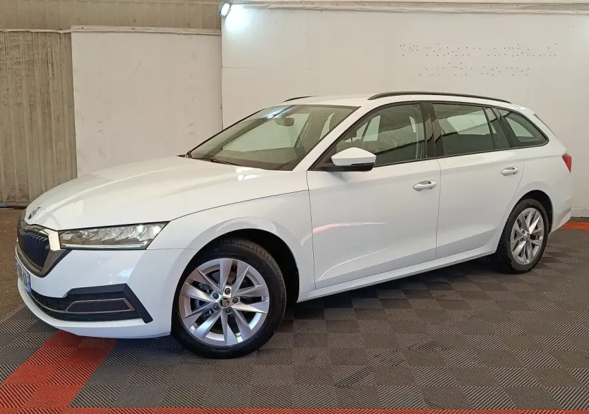 Skoda Octavia break blanc vue de profil droit en intérieur, avec jantes alliage et barres de toit noires.