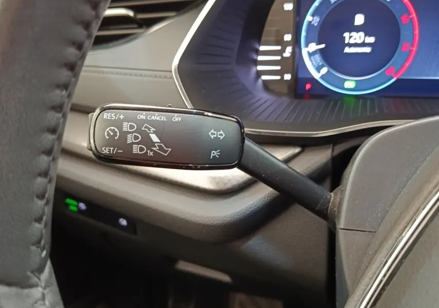 Gros plan sur la manette de régulateur de vitesse à gauche du volant dans l’habitacle sombre d’une Skoda Octavia blanche.