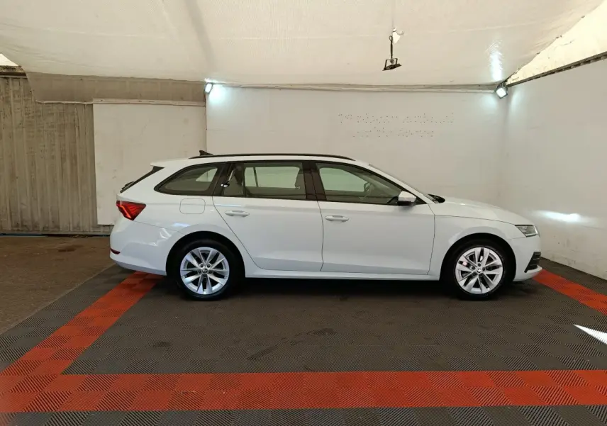 Vue de profil côté gauche d'une Skoda Octavia break blanche 2023 dans un garage avec rails de toit noirs.