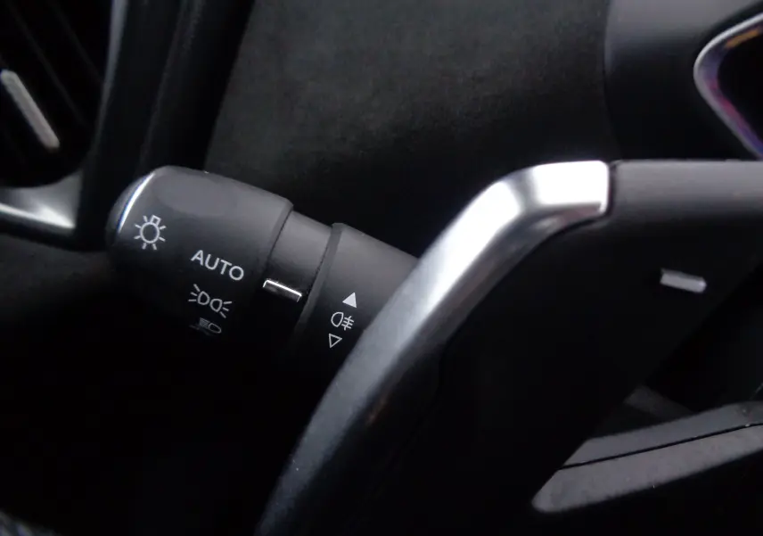 Gros plan sur la manette de feux automatique à gauche du volant dans l'habitacle noir du DS3 Crossback blanc banquise.