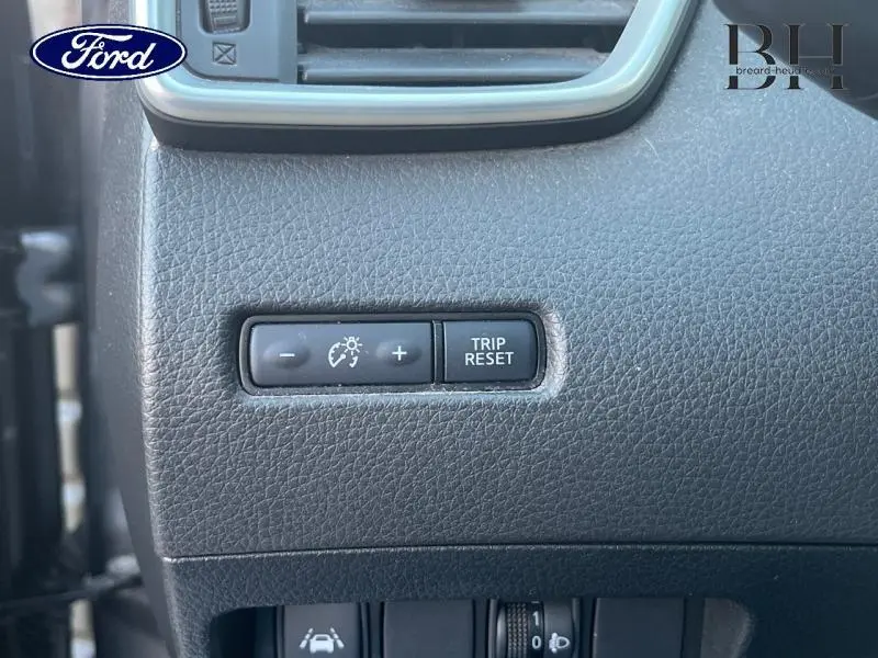 Gros plan sur les boutons de réglage d'éclairage et remise à zéro du compteur, tableau de bord gris foncé.