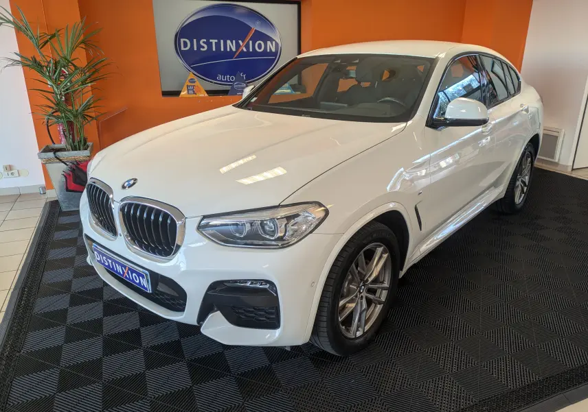 BMW X4 blanc en 3/4 avant droit dans un showroom avec jantes alliage et calandre chromée distinctive.