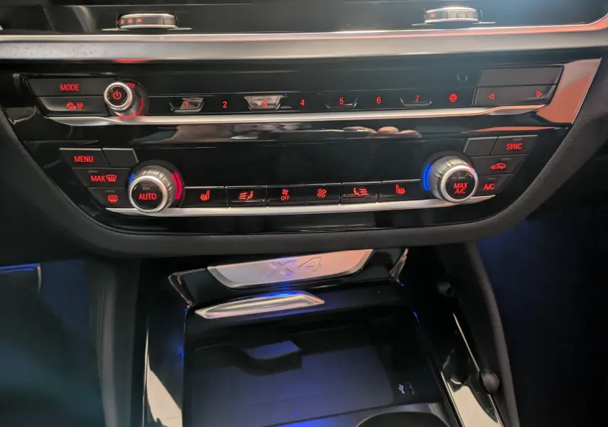 Vue rapprochée de la console centrale du BMW X4 blanc 2021, mettant en valeur les commandes de climatisation et le logo X4 rétroéclairé.