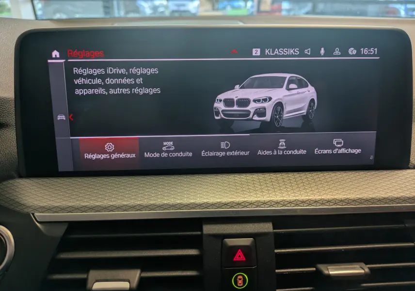 Écran central affichant les réglages du BMW X4 blanc vu en 3/4 avant droit sur l'interface iDrive.