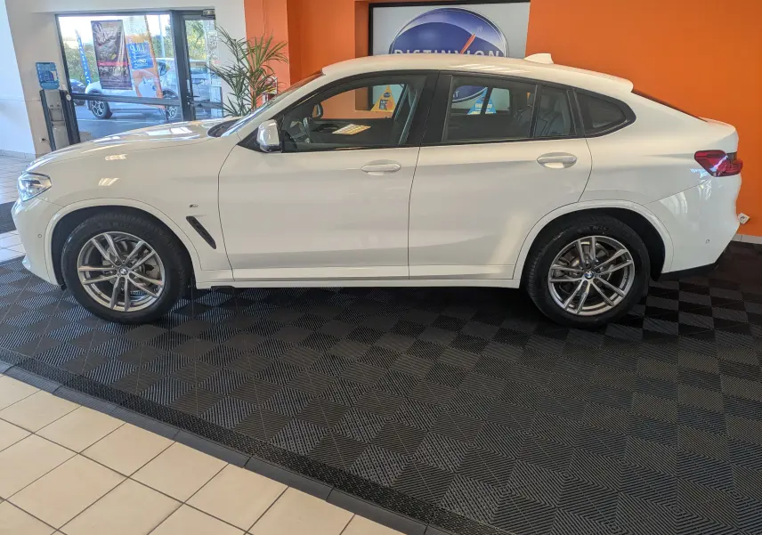 BMW X4 blanc en vue profil côté gauche, soulignant ses jantes alliage et silhouette sportive en intérieur showroom.