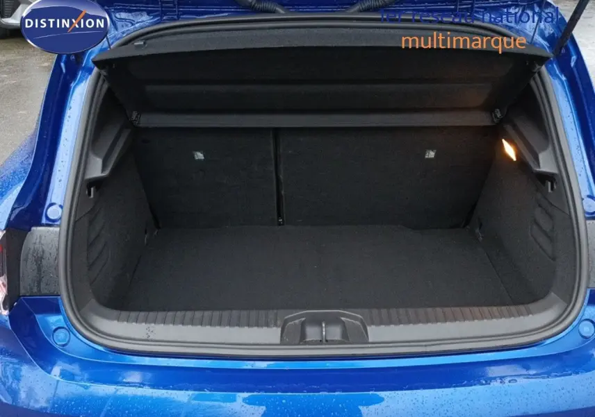 Coffre ouvert vu de l'arrière d'une Renault Clio 1.6 E-TECH bleu Iron Metal, intérieur noir et éclairage latéral.